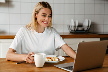 Obraz na płótnie Canvas Happy woman smiling and using laptop while having breakfast at home
