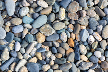 Top view of colored large pebbles. The texture of the pebble beach in sunlight.