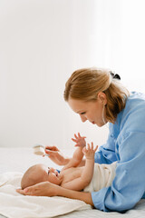 White blonde woman brushing and swaddling her baby in bedroom