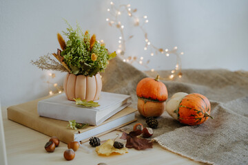 Autumn composition of books, pumpkins, nuts, autumn leaves, a bouquet of dried flowers, cones. Pumpkin and nuts. Garland with warm light. Bokeh. Thanksgiving Day. Festive composition.
