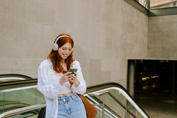 Young white woman smiling and using cellphone while walking outdoors