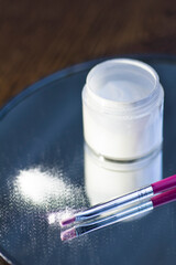 White acrylic powder to strengthen the nail plate and a brush in the reflection of the mirror