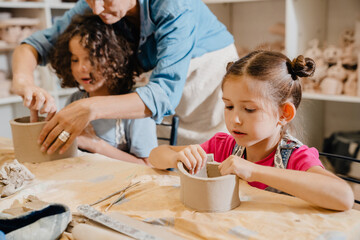 Cute kids sculpting clay crafts at table in pottery class - obrazy, fototapety, plakaty