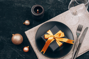 Christmas and New Year table setting in black. Black plate, cutlery, gift box, candle, wineglass and toys. Top view