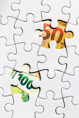 Money is found in the missing pieces of a jigsaw puzzle. 100 and 50 euros were found by solving the financial challenge and in the crisis
