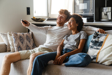 Young beautiful happy smiling interracial couple watching tv together