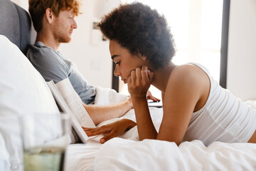 Young beautiful african woman reading lying with her working boyfriend