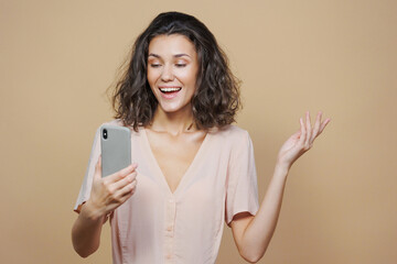 beautiful woman in beige holds a smartphone in her hand and makes a gesture with her hands surprise love and joy, selling an advertising poster. the woman in the background smiles and laughs. a model