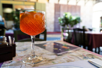 A large faceted glass with an Aperol cocktail stands on a table outside in a cafe in the old town without tourists