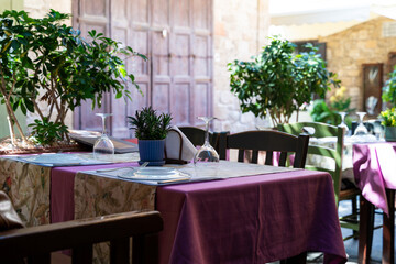 Beautiful table setting in a street cafe in an old town. On a table covered with a purple tablecloth are wine glasses, a plate and cutlery.