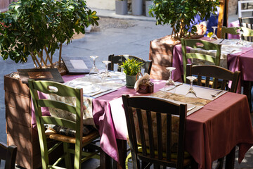 Beautiful table setting in a street cafe in an old town. On a table covered with a purple tablecloth are wine glasses, a plate and cutlery.
