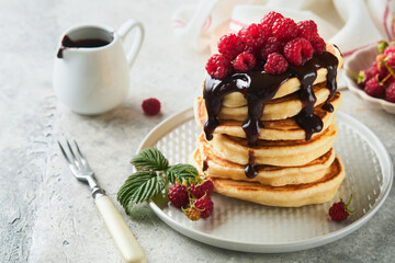 American pancakes. Stack pancakes with fresh raspberry with chocolate glaze or toppings in white bowl on light gray table background. Homemade classic american pancakes. Magazine concept. Top view.