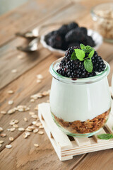 Fototapeta na wymiar Yogurt with granola, blackberry berry fruits and muesli served in glass jar on wooden background. Healthy breakfast concept. Healthy food for breakfast, top view