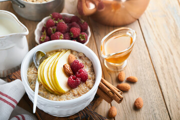 Oatmeal. Bowl of oatmeal porridge with raspberry, pear and honey on old wooden table background. Hot and healthy food for Breakfast, top view, flat lay