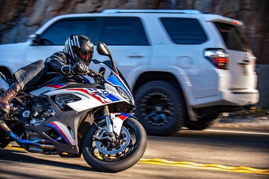 Rider on a BMW S1000RR M motorcycle in motion with a car in the  blurred background