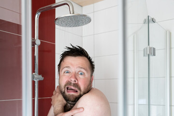 Man in the shower under cold water, he freezes and looks miserable. Energy crisis concept.