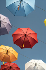 Street scenery from open multi-colored umbrellas suspended above ground to decorate city and create shade from hot summer sun. Urban art object with parasols protecting from sunlight under blue sky