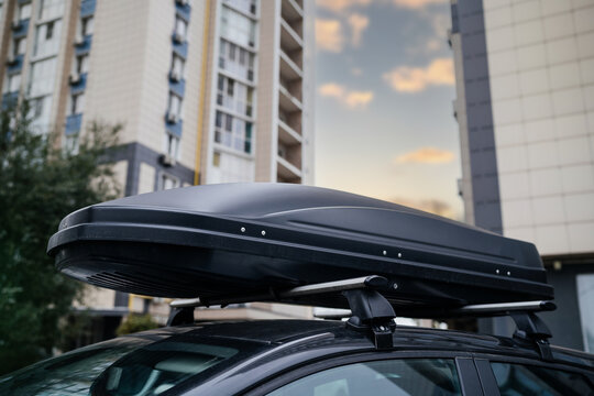 Big Black Box Of Luggage Rack On The Roof Of A Black Car. Travel And Transportation Accessories.