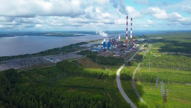 Top view of power plant on lake shore. Clip. Factory pipes on background of lake and green forest. Landscape with power station and pipes by lake in summer