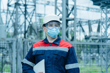 Fototapeta na wymiar A masked power engineer during a pandemic inspects the modern equipment of an electrical substation before commissioning. Energy and industry. Scheduled repair of electrical equipment.