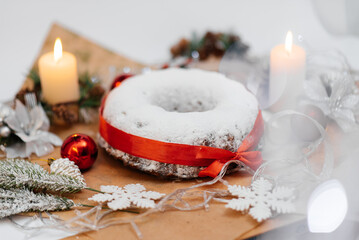 Traditional round Christmas stollen made of dried fruits and nuts, sprinkled with powdered sugar on the background of a Christmas decor with candles. A festive treat.