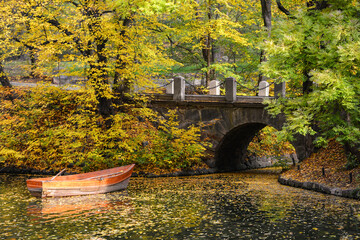 Ancient stone bridge in the autumn National Dendrology Park of Sofiyivka, Uman, Ukraine. Pleasure boat on the water.