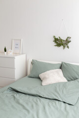 Winter bedroom decor. Christmas home decor. New year interior decorations. Coniferous branch on white wall, bed with green linen, frame with text HELLO WINTER on chest of drawers.