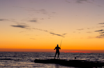 silhouette of  man on  pier by  sea against  sunset.  male fisherman holds  fishing rod,  beautiful seascape.  lonely man.