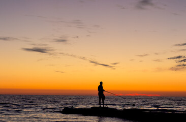 silhouette of  man on  pier by  sea against  sunset.  male fisherman holds  fishing rod,  beautiful seascape.  lonely man.