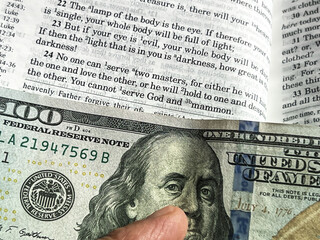 The Holy Bible in English with a tab from the $ 100 banknote showing a passage from the Gospel...