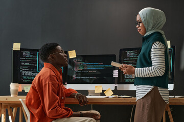 Two young confident multicultural interns in casualwear looking at each other during discussion of...