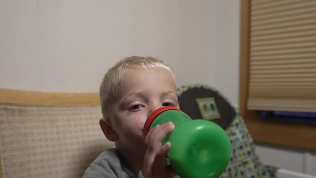 Handheld close up of a young toddler drinking milk out of a sippy cup green bottle. Slow motion