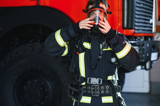 Firefighter portrait on duty. Photo fireman with gas mask and helmet near fire engine.