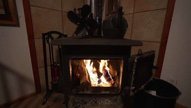Wide angle view of woodstove fireplace with heat fan and iron kettle. Fire in slow motion