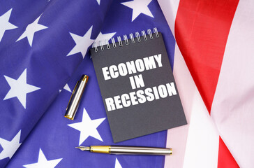 On the American flag lies a pen and a notebook with the inscription - Economy in recession