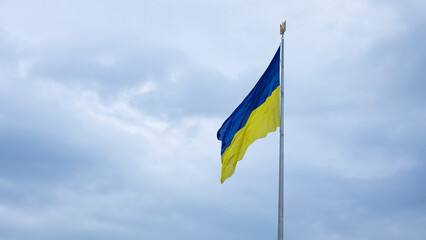 The Ukrainian flag of blue and yellow national colors on the flagpole flutters in the wind against the blue sky and the morning rising sun. The official state symbol of Ukrainians. Patriotism.