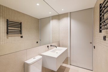 Interior of modern bathroom with large mirror, beige tiles, black radiator and white sink