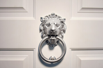 Head of a lion in silver color for knocking on a white door. Knocker in the form of a muzzle of a...