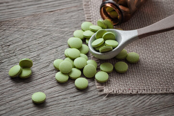 Lots of scattered green pills on a wooden background,  dietary supplement