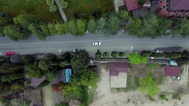 4k Top view of cars drive along road in countryside irrl. Above shot for transport rides along street with modern houses and green trees on summer day. Operator uses flying drone and films
