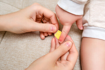 Woman mother sticks a medical band-aid on the toddler baby finger. Mom s hand with a sticky wound...