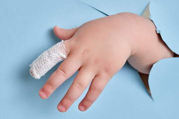 Baby s hand with a bandaged finger on a blue studio background, close-up. Injured index finger of a child wrapped in a white bandage. Kid boy aged one year and three months