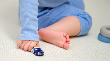 Toddler baby boy is playing with toy cars on the floor in the home room. A child plays with toys in...