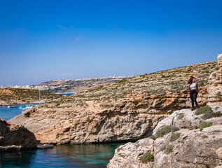 woman standing on the edge of the cliff, admire the sea in comino island, malta