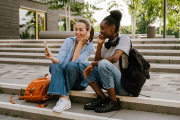 Young multinational girls talking and using cellphone together outdoors