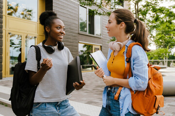 Young multiracial women talking while standing by campus outdoors