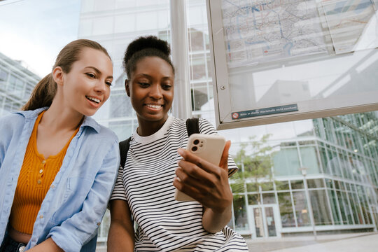 Multiracial Women Using Mobile Phone Together While Sitting At Bus