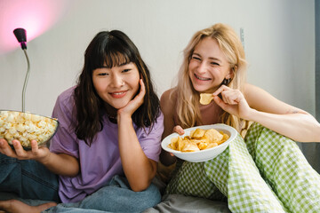 Two multiracial girls eating snacks while watching movie together
