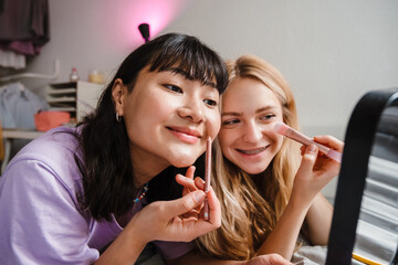 Two multiracial girls smiling and doing makeup at home