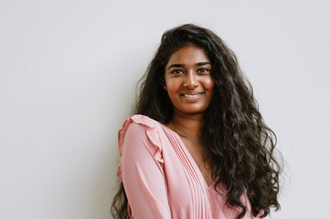 Fototapeta premium Young indian woman smiling and looking at camera while standing by wall
